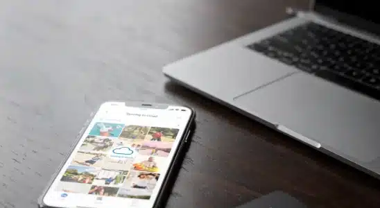 Smartphone resting beside a laptop and external drive showing photo backup progress