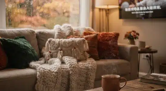 A cozy living room setup with blankets, warm drinks, and a TV playing on a rainy fall day