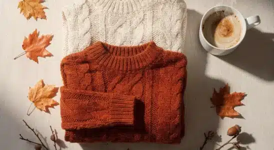 Folded neutral knit sweaters displayed with a warm drink on a rustic table