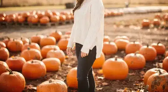 Woman wearing a cozy sweater and boots posing in a pumpkin patch.