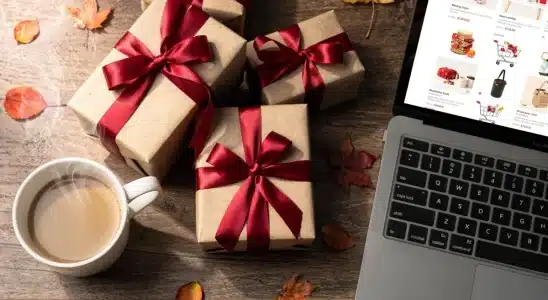 Holiday gift boxes wrapped in festive paper next to a laptop displaying early seasonal sales.