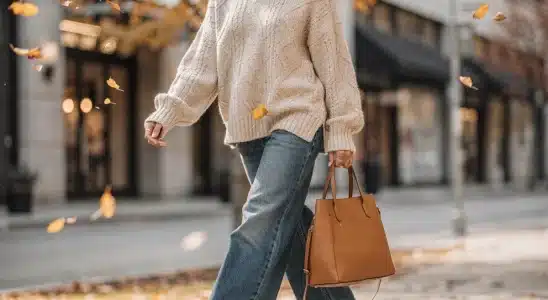 Woman wearing a cozy beige sweater and wide-leg jeans walking on an autumn sidewalk