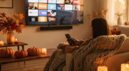 Person holding a TV remote choosing streaming apps in a cozy fall living room
