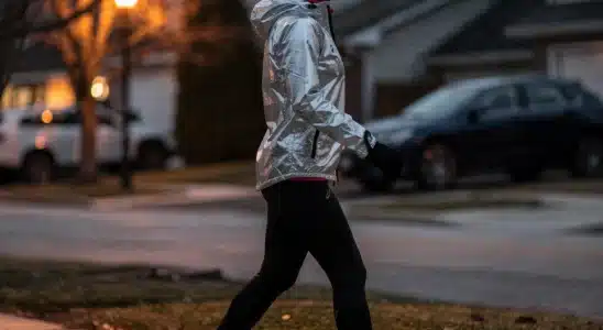 Woman walking outside at dusk wearing reflective winter workout gear.